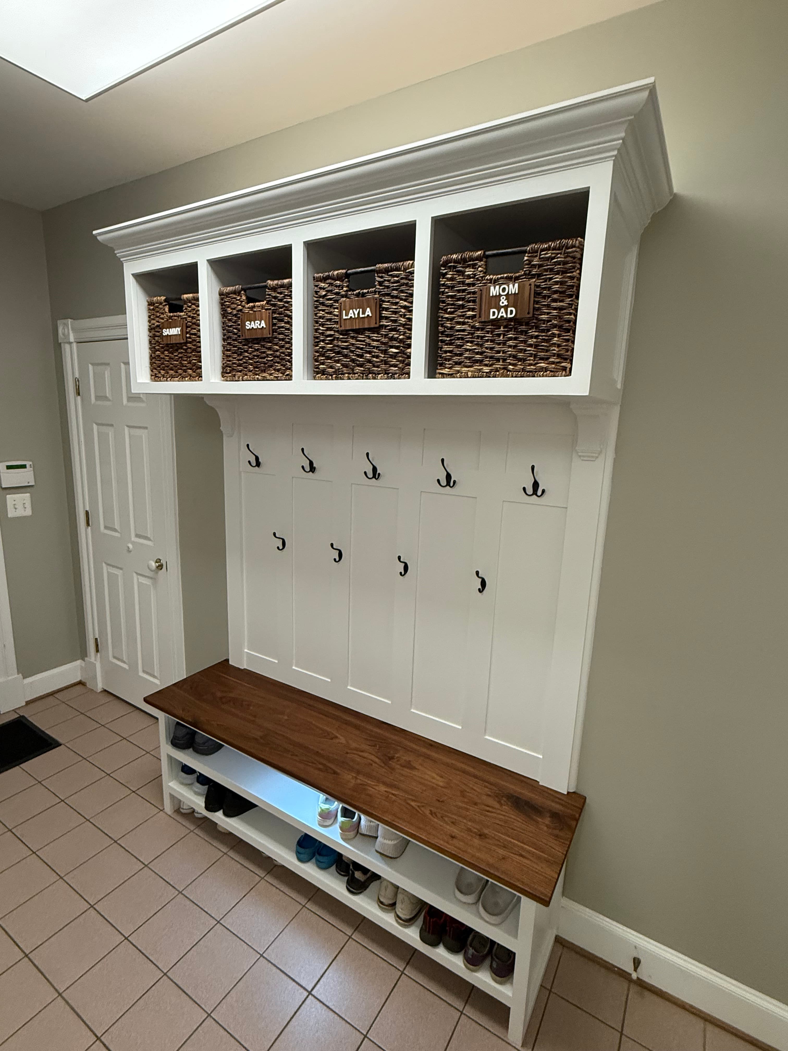 Custom white mudroom cabinetry with woven baskets, coat hooks, and a warm wooden bench